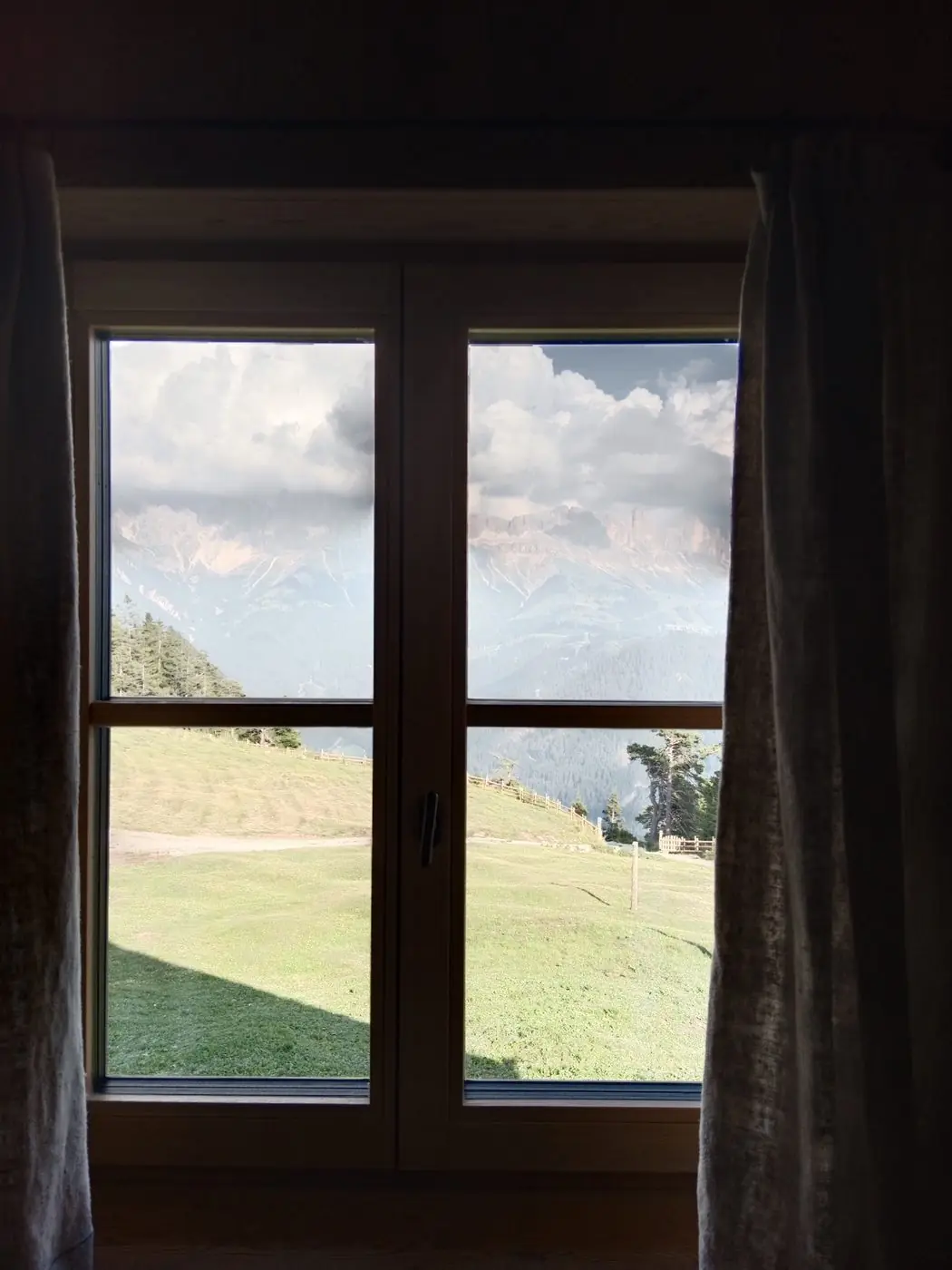 Blick aus einem Almhaus-Fenster auf Berge und Wiese