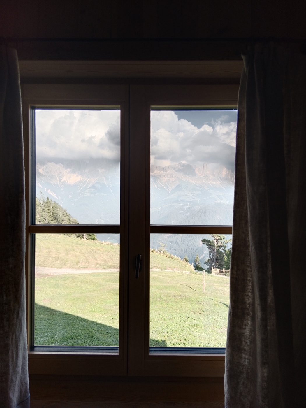 Blick aus einem Almhaus-Fenster auf Berge und Wiese